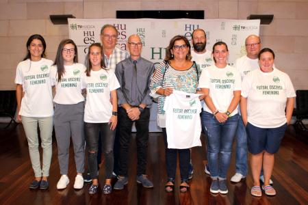 Imagen: Elisa Sancho con jugadoras y directivos, detrás el lema Huesca la Magia